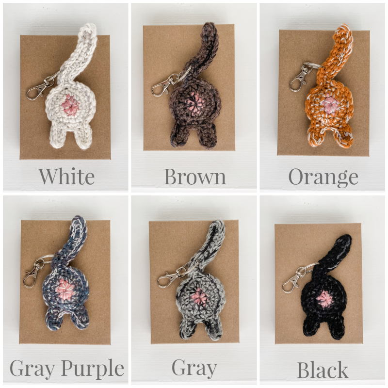 collage of white, brown, orange, gray purple, gray, and black crocheted cat butt keychains on Kraft boxes