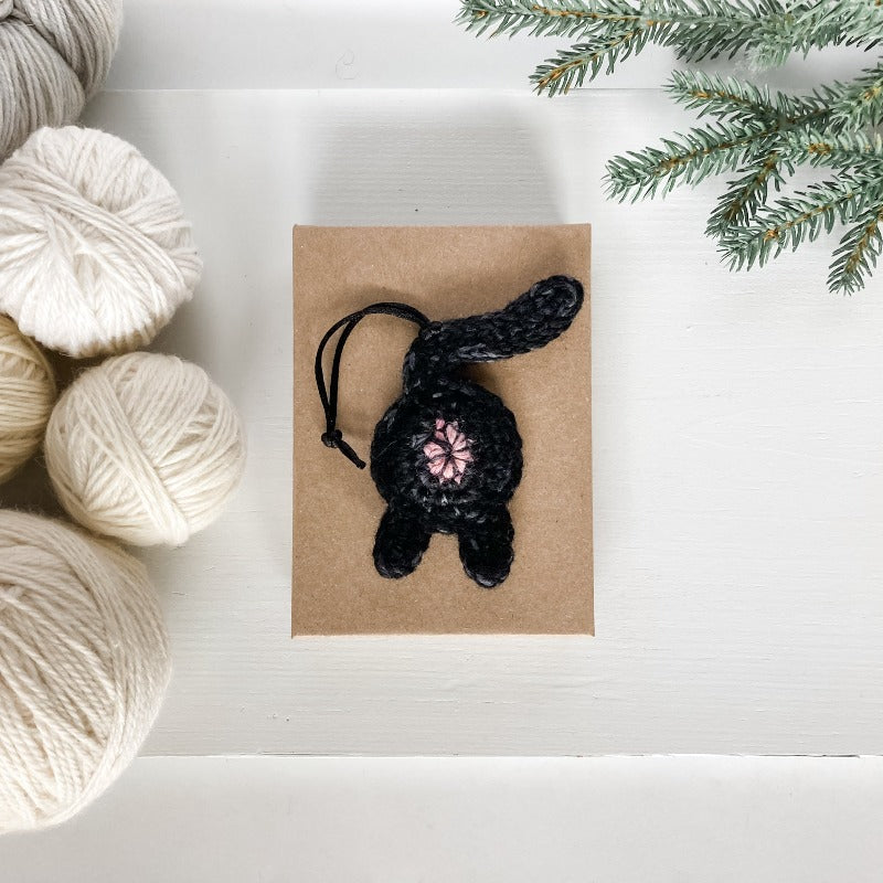 crocheted black cat butt ornament on a Kraft box next to white and ecru yarn