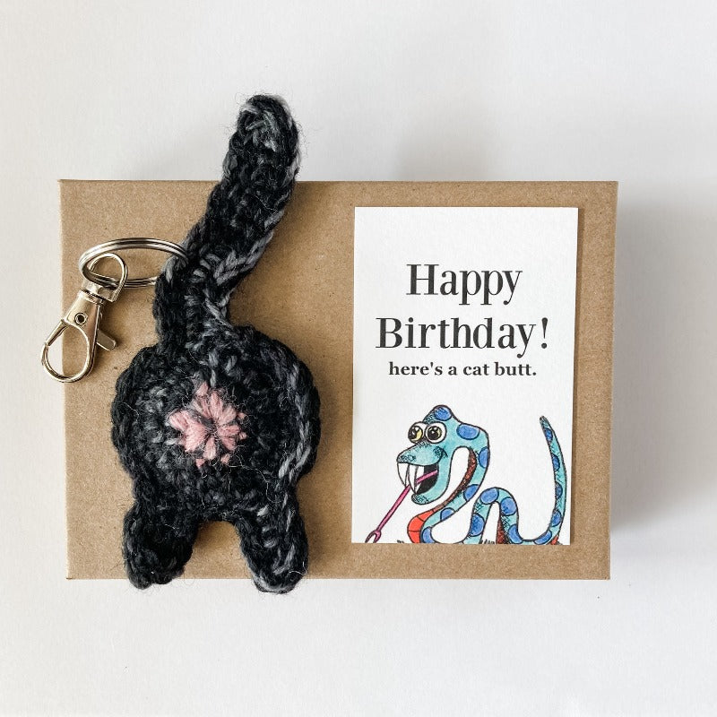 black cat butt keychain and illustrated snake birthday card on a Kraft box